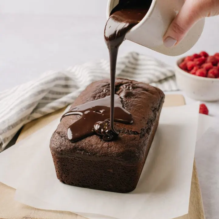 pouring chocolate ganache over chocolate cake on wooden board