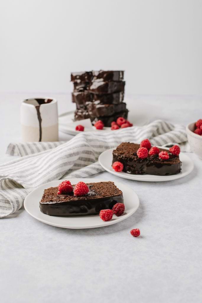 slice of chocolate yogurt cake with chocolate glaze and raspberries on two white plates
