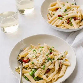 creamy pasta with boursin cheese and green peas in two white bowls with glasses of white wine