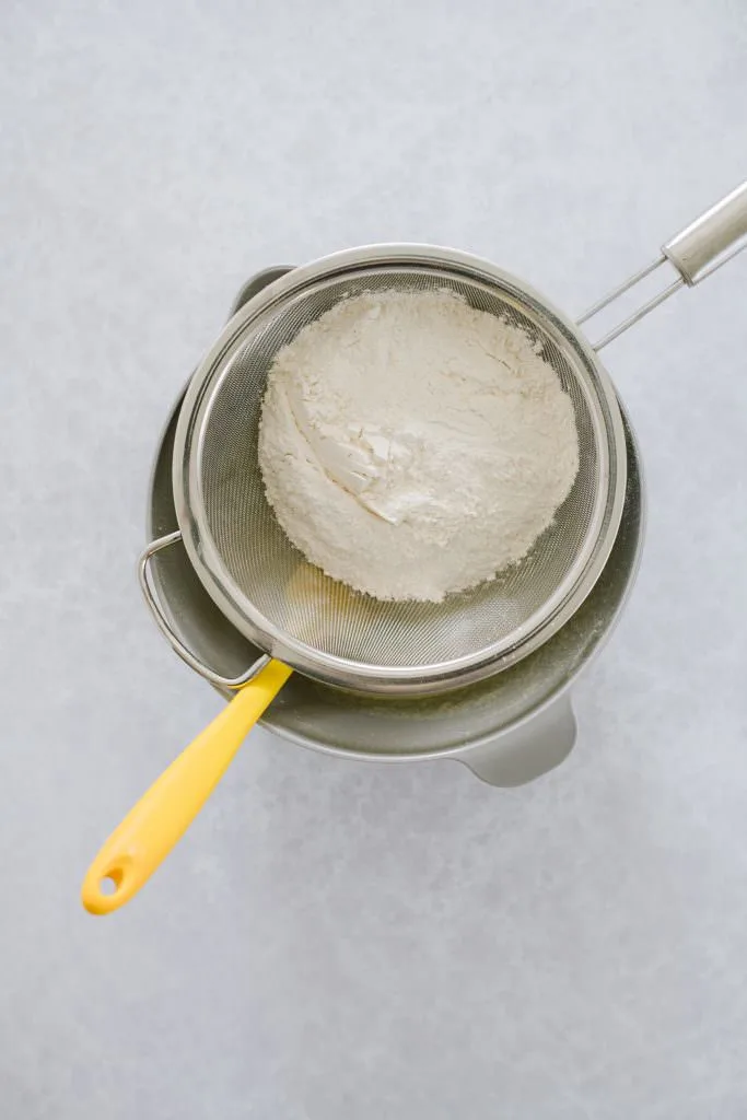 flour in sifter on top of mixing bowl with yellow spatula