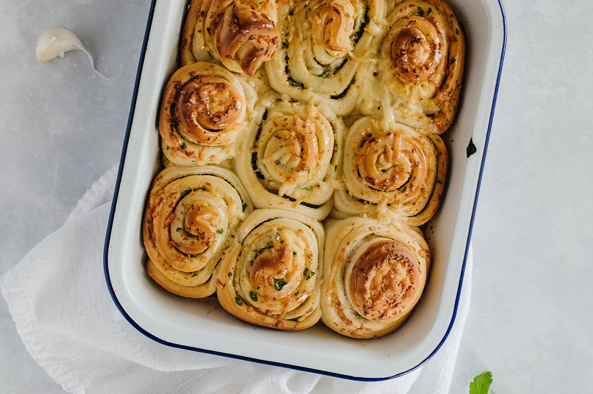 pan of garlic rolls on a white background with a clove of garlic and a parsely leaf on the side