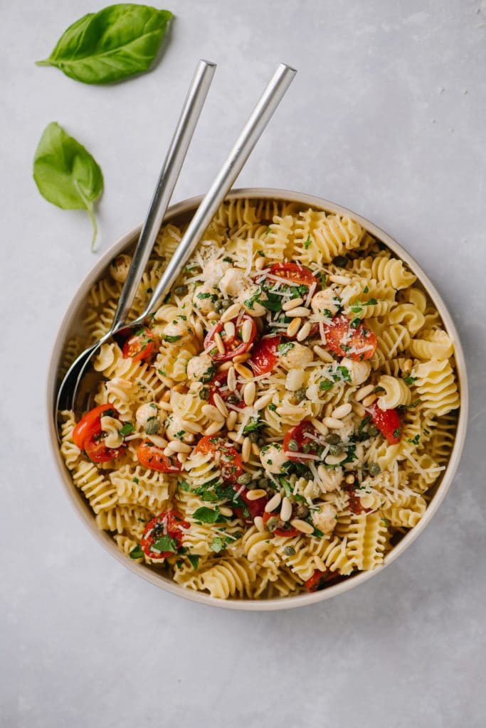 easy bruschetta pasta recipe in large white bowl with serving spoons and fresh basil leaves
