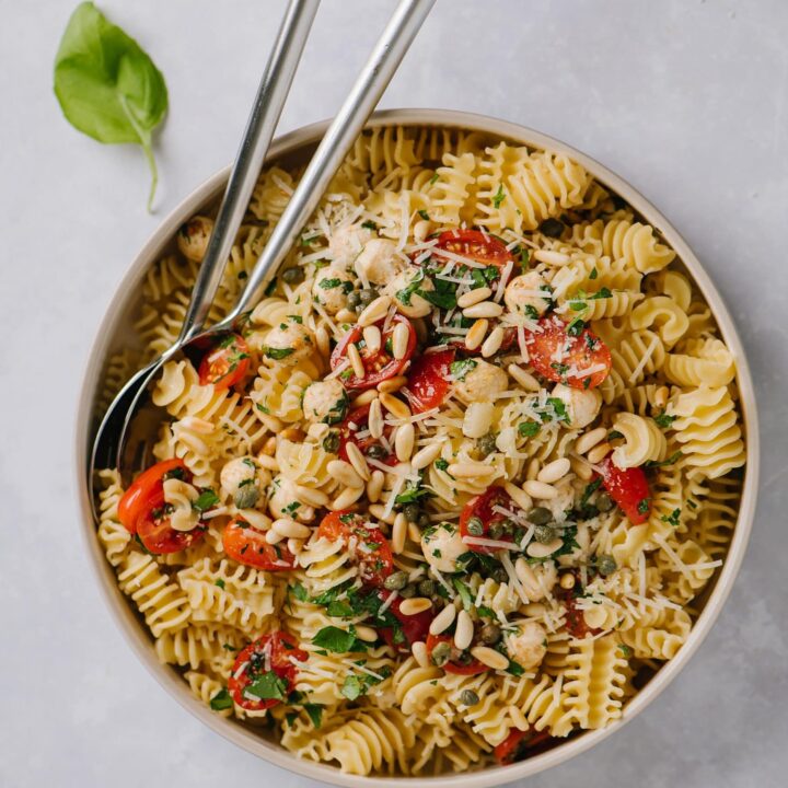 easy bruschetta pasta recipe in large white bowl with serving spoons and fresh basil leaves