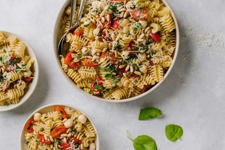 fresh tomato and basil pasta in large white bowl with basil leaves and two small bowls with fresh basil leaves
