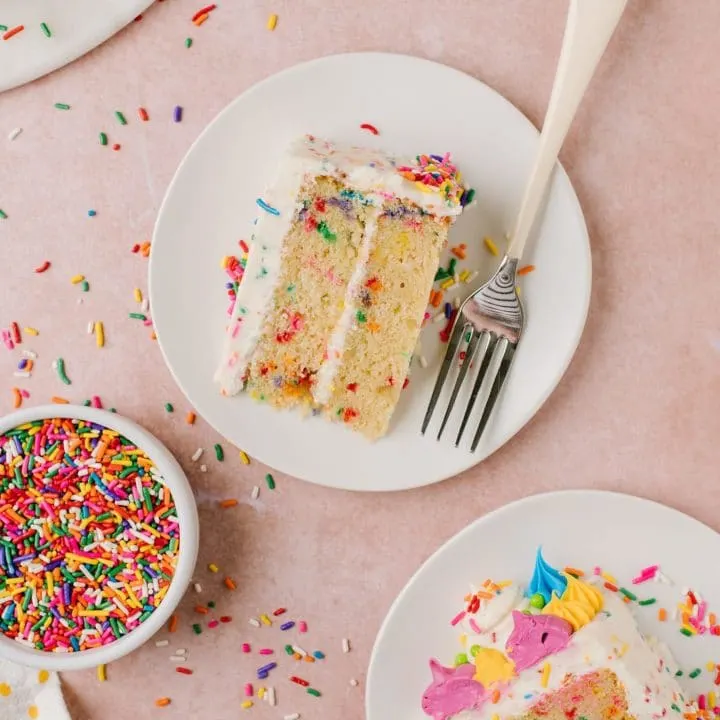 slices of vanilla cake with rainbow sprinkles on white plates with fork and sprinkles on side