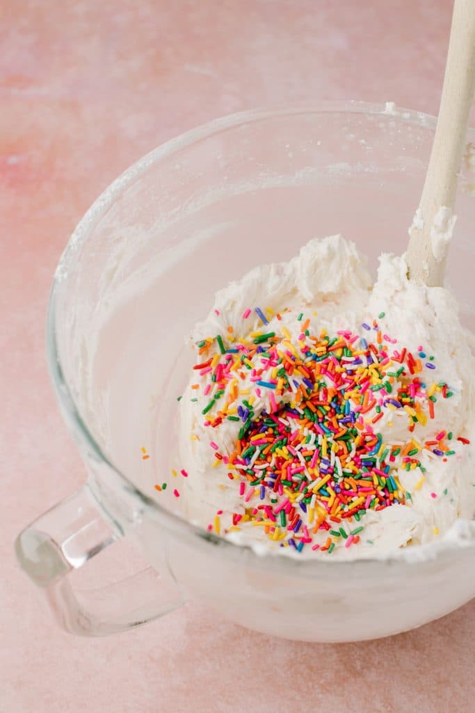vanilla cake batter and rainbow sprinkles in glass mixing bowl with spatula