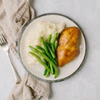 overnight chicken breasts with mashed potatoes and green beans on white plate with gray napkin and fork