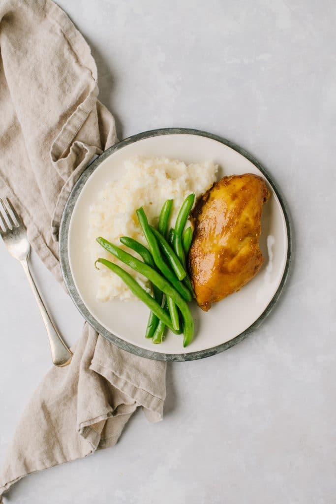 overnight chicken breasts with mashed potatoes and green beans on white plate with gray napkin and fork