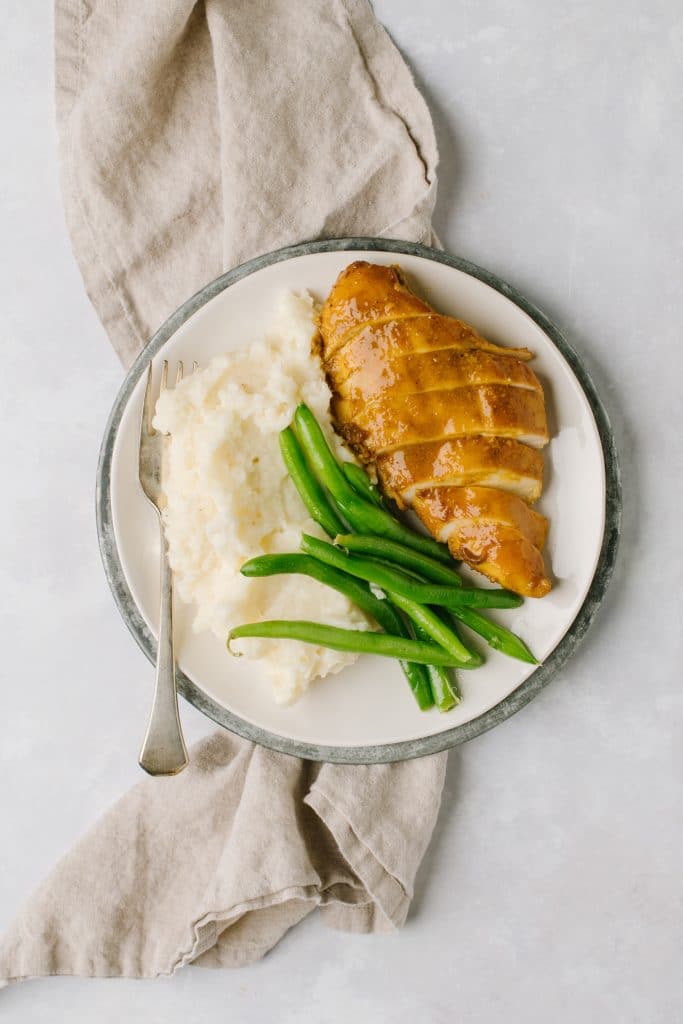 sweet and savory chicken breast with mashed potatoes and green beans on white plate with gray napkin and fork