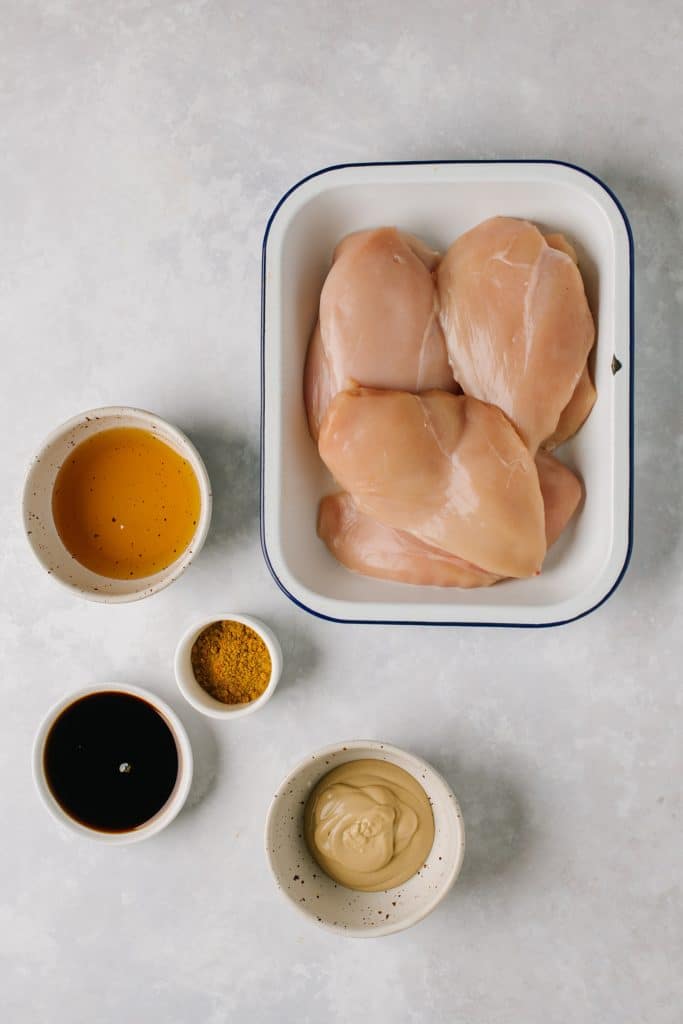 chicken breasts in ceramic dish, honey, soy sauce, curry powder, dijon mustard in bowls