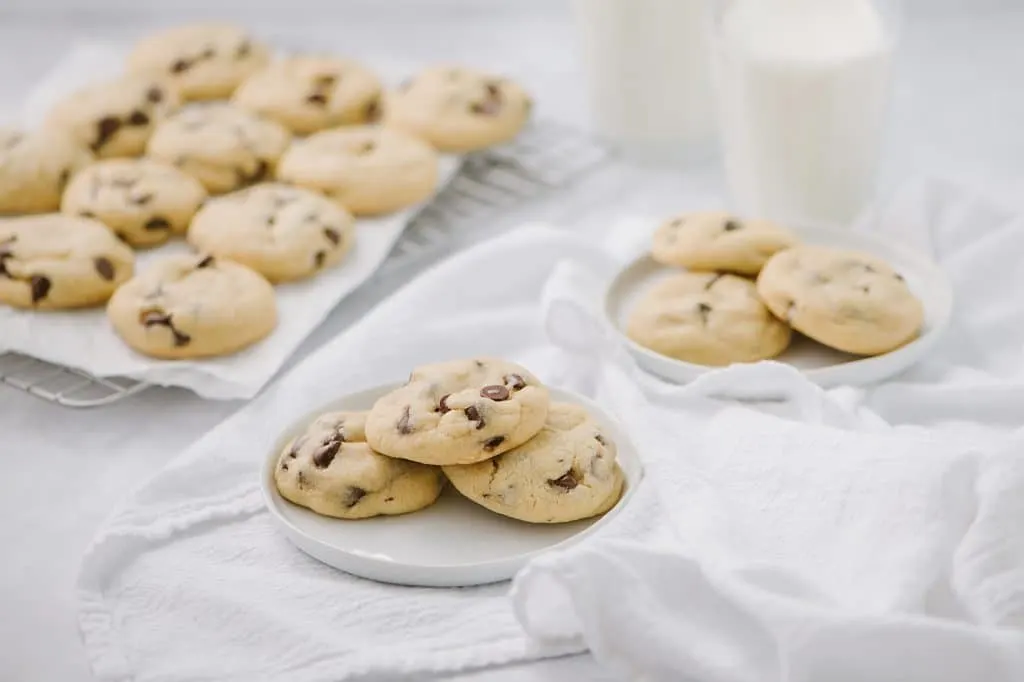 chewy chocolate chip cookies on white plates and platter with two glasses of milk