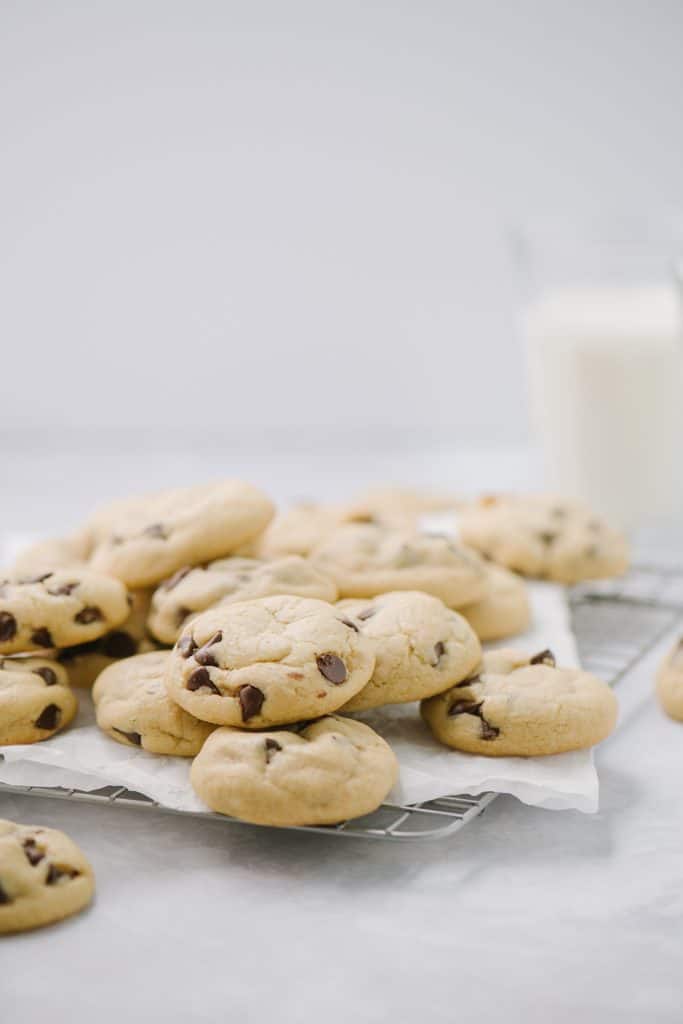 chewy chocolate chip cookies on white platter with glass of milk