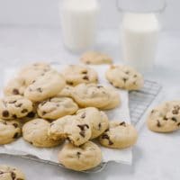 cookies with chocolate chips on cooling rack with two glasses of milk