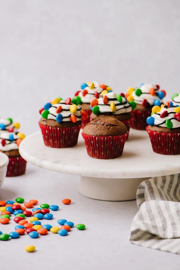 chocolate cupcakes decorated with vanilla frosting, black strings and m&ms on cake platter