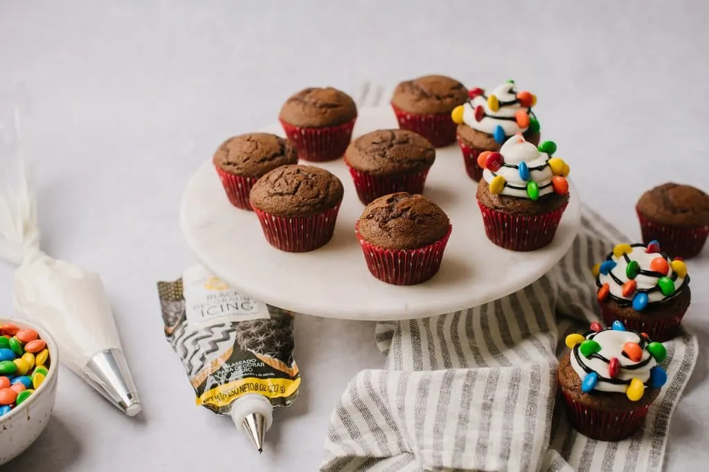chocolate cupcakes on wire rack with pastry bag filled with frosting and m&ms
