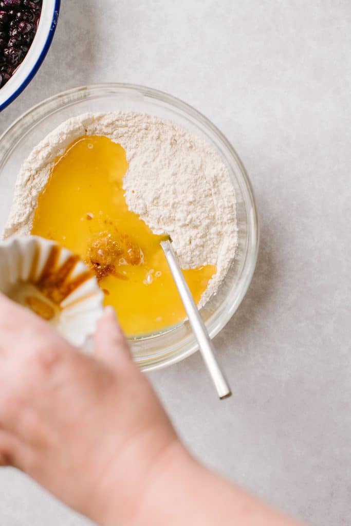 butter and vanilla being poured in a bowl of dry ingredients