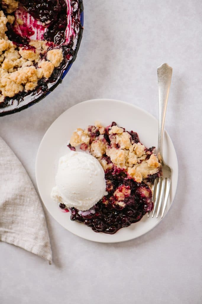 overhead shot of plate of blueberry crisp and vanilla ice cream with a fork 