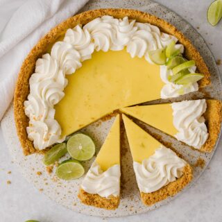 easy key lime pie recipe topped with whipped cream and sliced with fresh limes on the side