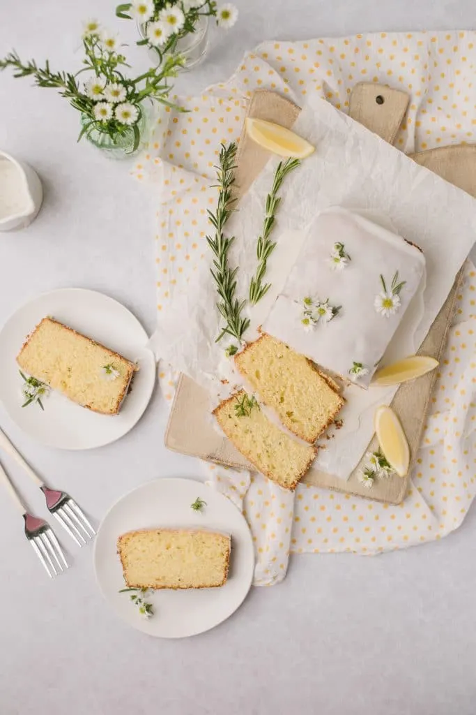 lemon cake sliced on white plates with forks and rosemary sprigs