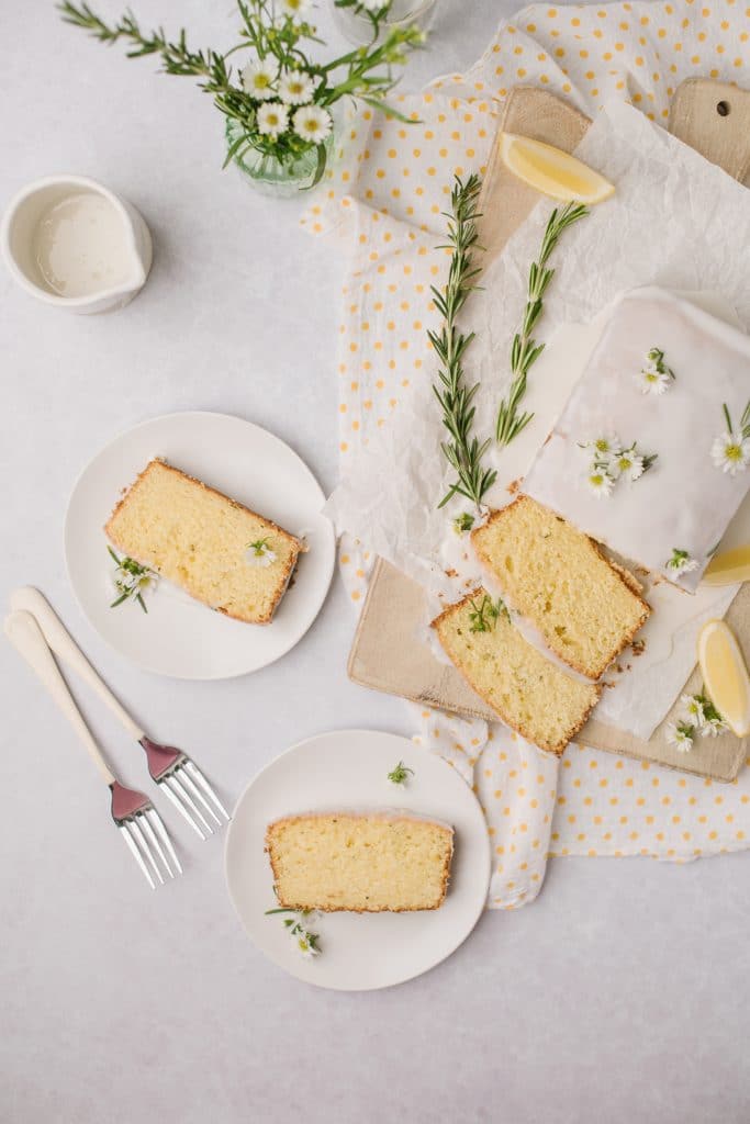 lemon cake sliced on white plates with forks and rosemary sprigs