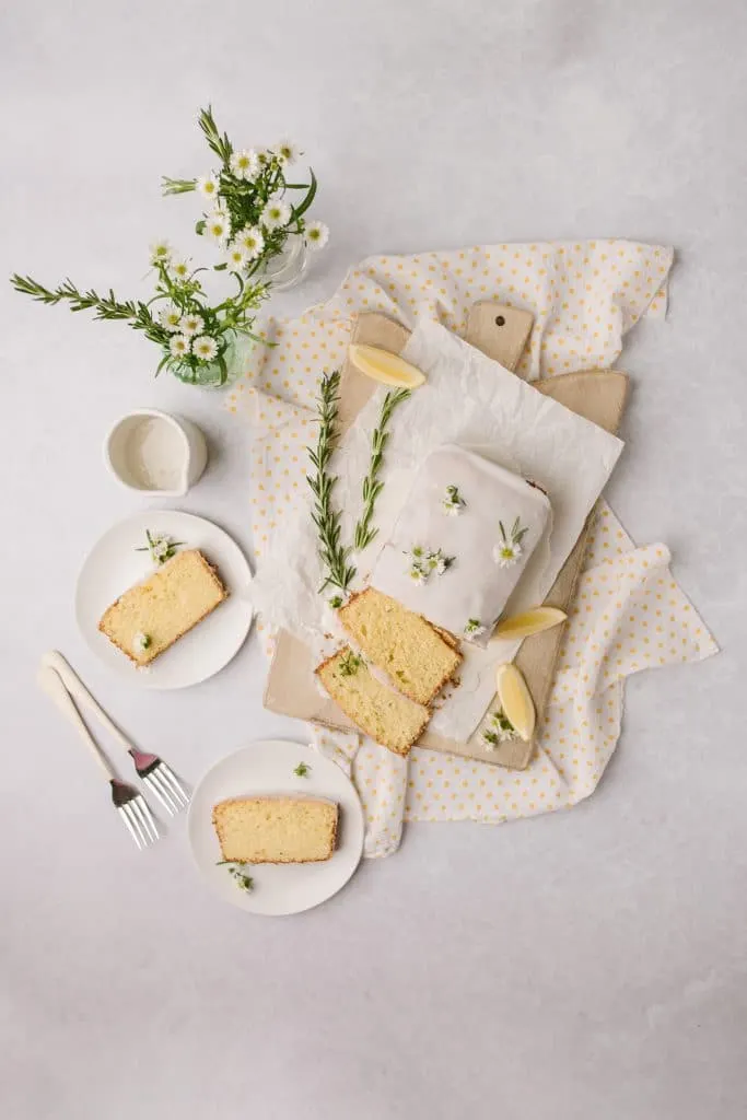 lemon and rosemary cake recipe sliced on white plates with forks and rosemary sprigs