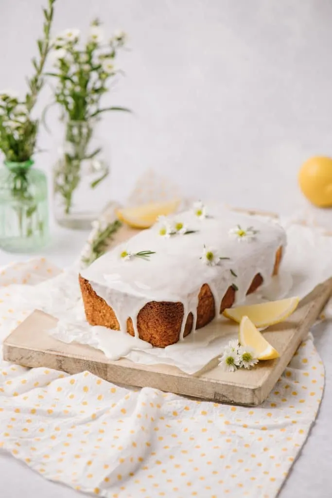 moist lemon cake with lemon glaze on wooden board with fresh lemon slices and rosemary sprigs