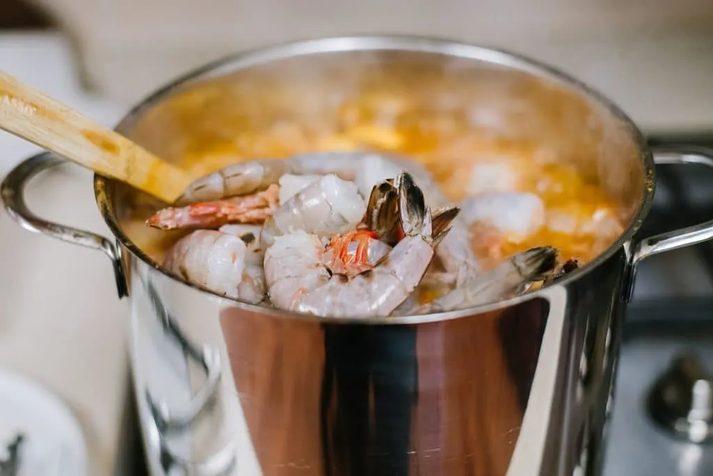 raw shrimp in large stockpot with stock and vegetables