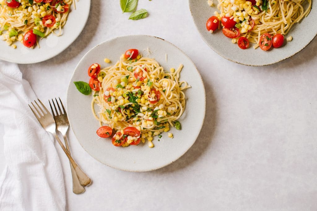 A plate of Pasta with Sweet Corn Gremolata and two forks on the side with two plates of pasta just out of frame