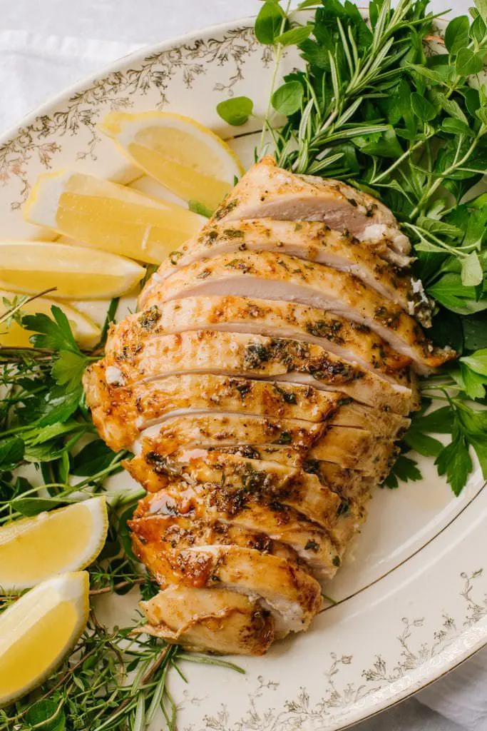 easy brined turkey breast sliced on white platter with lemon wedges and fresh herbs
