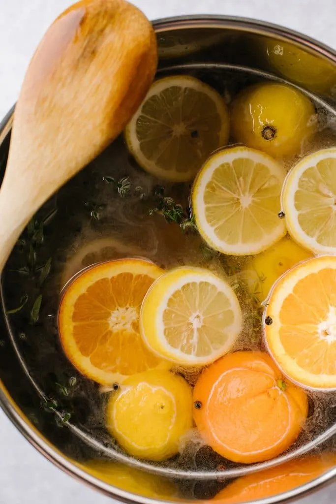 fresh lemon and orange slices in pot with brine solution and wooden spoon