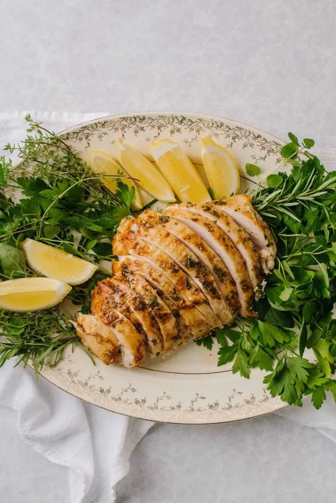 best brined turkey sliced on white platter with lemon wedges and fresh herbs
