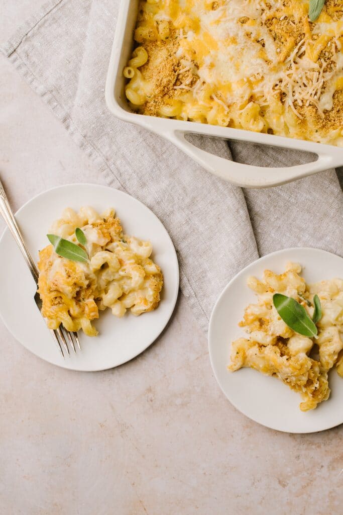 butternut macaroni and cheese on two white plates garnished with sage