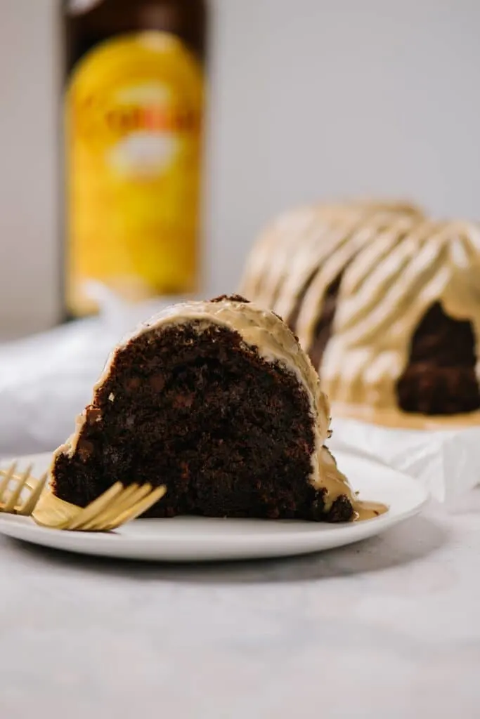 slice of chocolate cake with kahlua glaze on white plate with kahlua bottle and cake in background