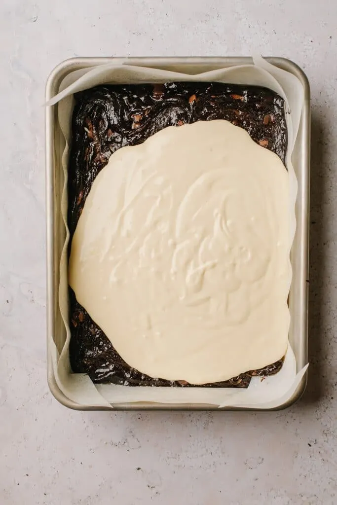 cheesecake batter spread over brownie batter in baking dish