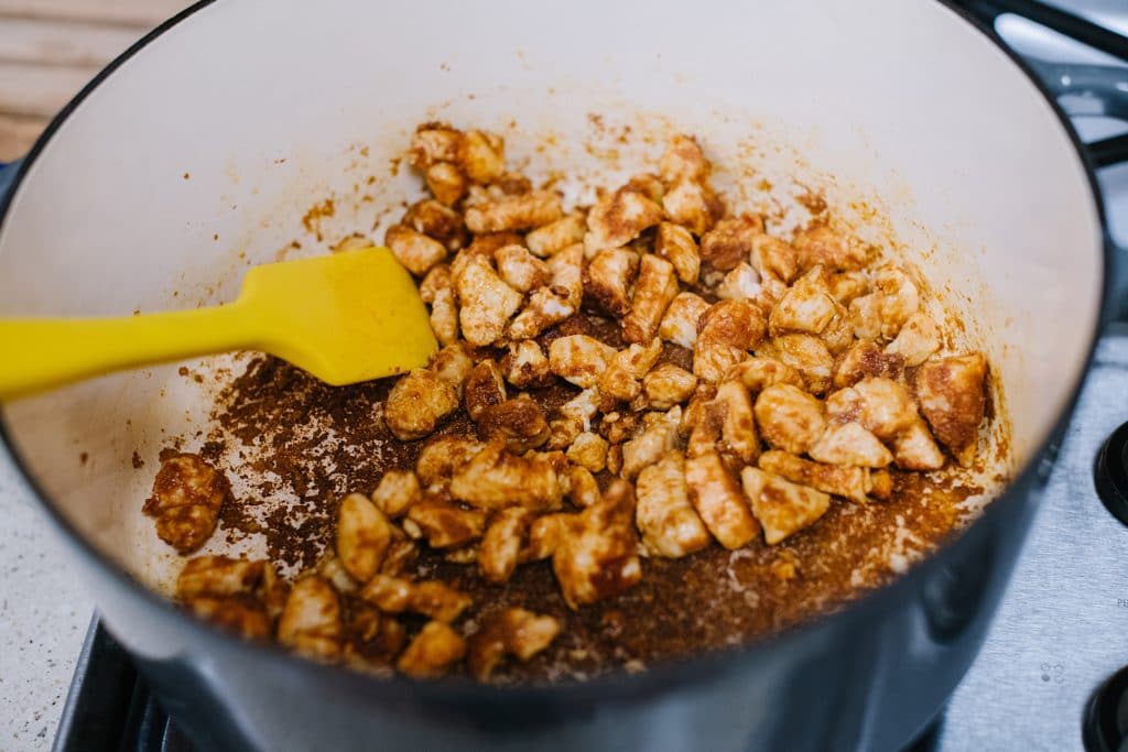 sauteeing chicken and Mexican spices in pot with yellow spatula