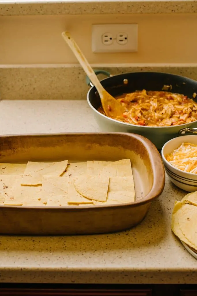quartered corn tortillas in baking dish with chicken and tomato filling in skillet