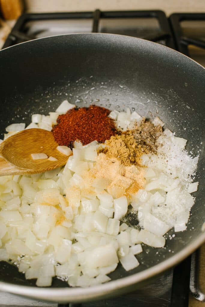chile powder, cumin and garlic powder with softened onions in skillet
