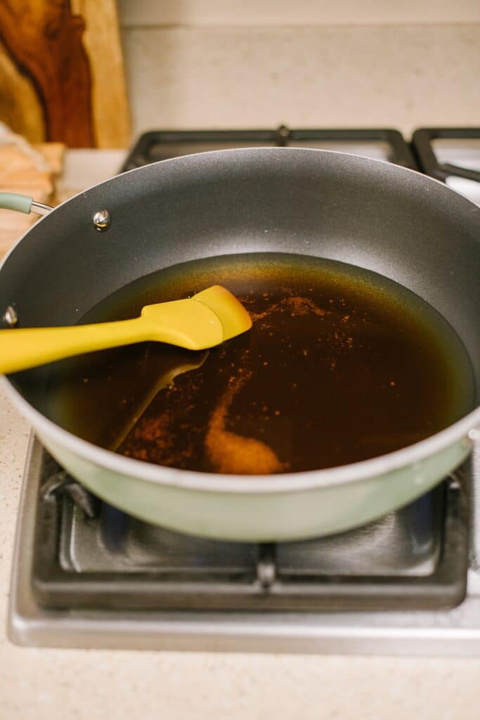 maple syrup and water in nonstick skillet on stove with yellow spatula