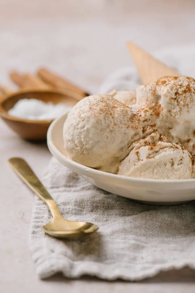 scoops of no churn ice cream recipe topped with cinnamon with cone in white bowl and spoon on side