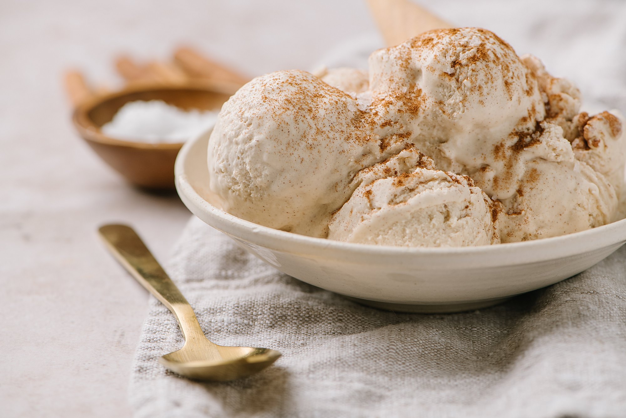 scoops of no churn ice cream recipe topped with cinnamon with cone in white bowl and spoon on side