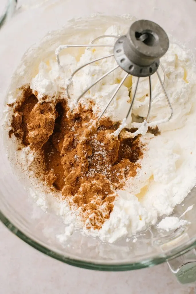 cinnamon sprinkled over whipped cream in glass bowl