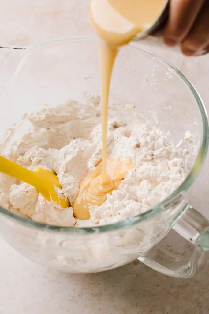 pouring sweetened condensed milk in whipped cream in glass bowl