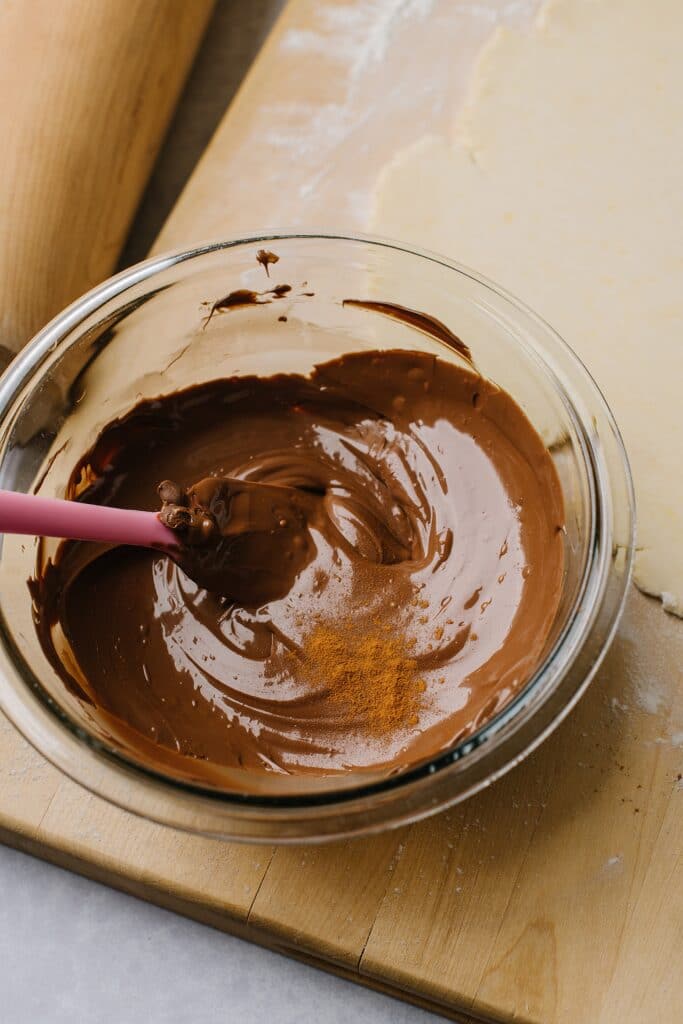 A bowl of melted chocolate, topped with a hefty scoop of cinnamon which is about to be mixed in.