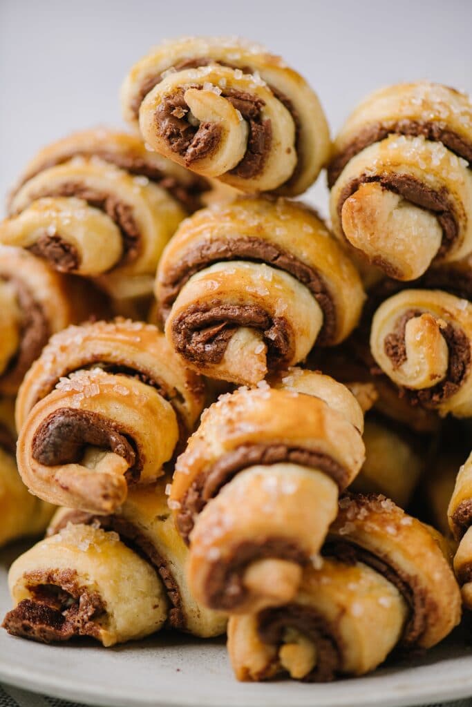A close up shot of a pile of chocolate cinnamon rugelachs, with crispy edges and flakes of sugar.