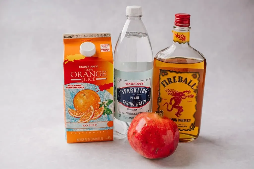 A picture of the four ingredients for this drink - orange juice, Fireball whiskey, pomegranate, and seltzer