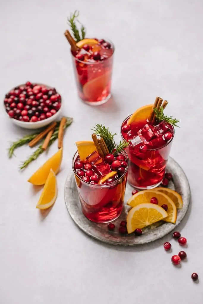 Glasses of mulled red wine sangria, surrounded by fresh cranberries and oranges. 
