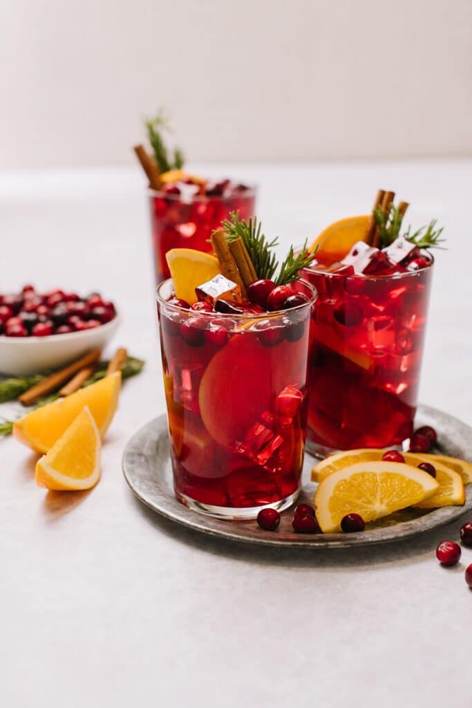 Glasses of mulled red wine sangria, garnished with oranges and rosemary sprigs, on a silver platter.