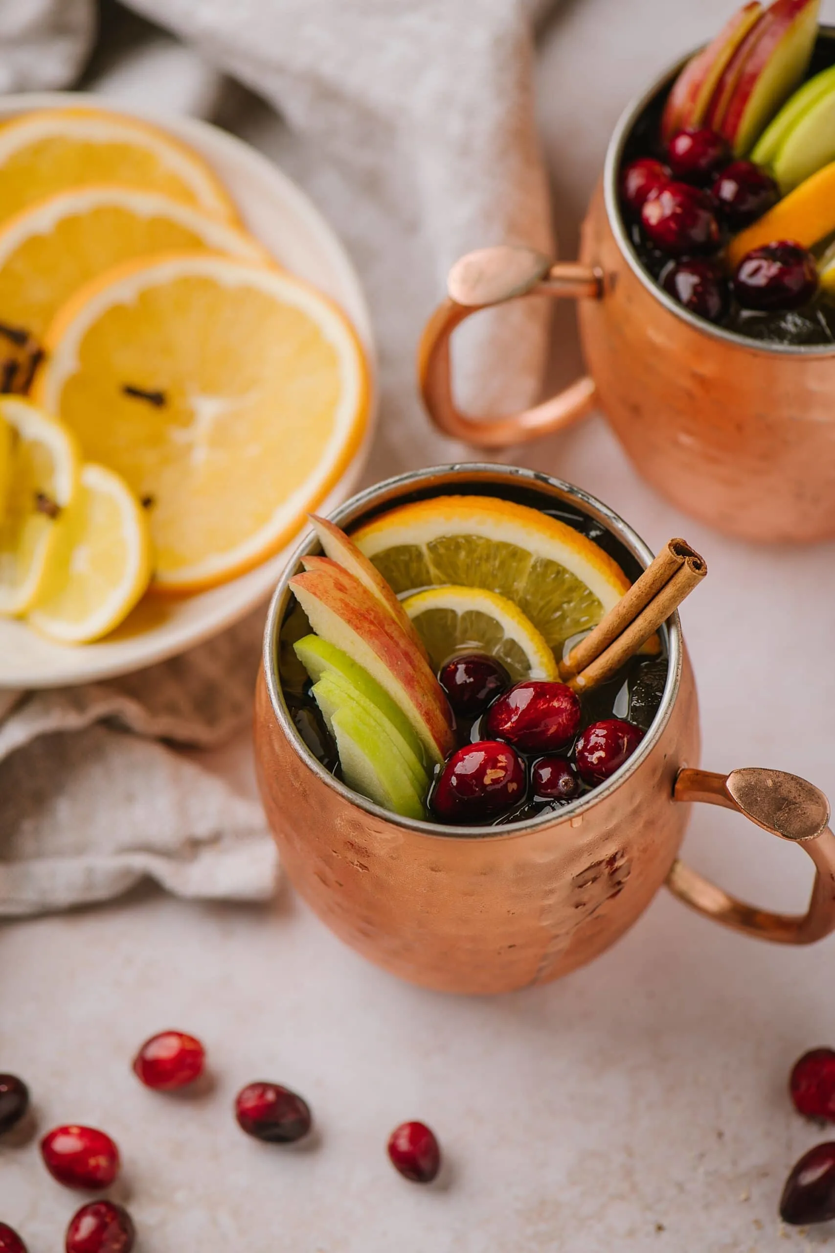 An overhead shot of a chilled spiced apple cider cocktail with cranberries, fruit, and cinnamon sticks.