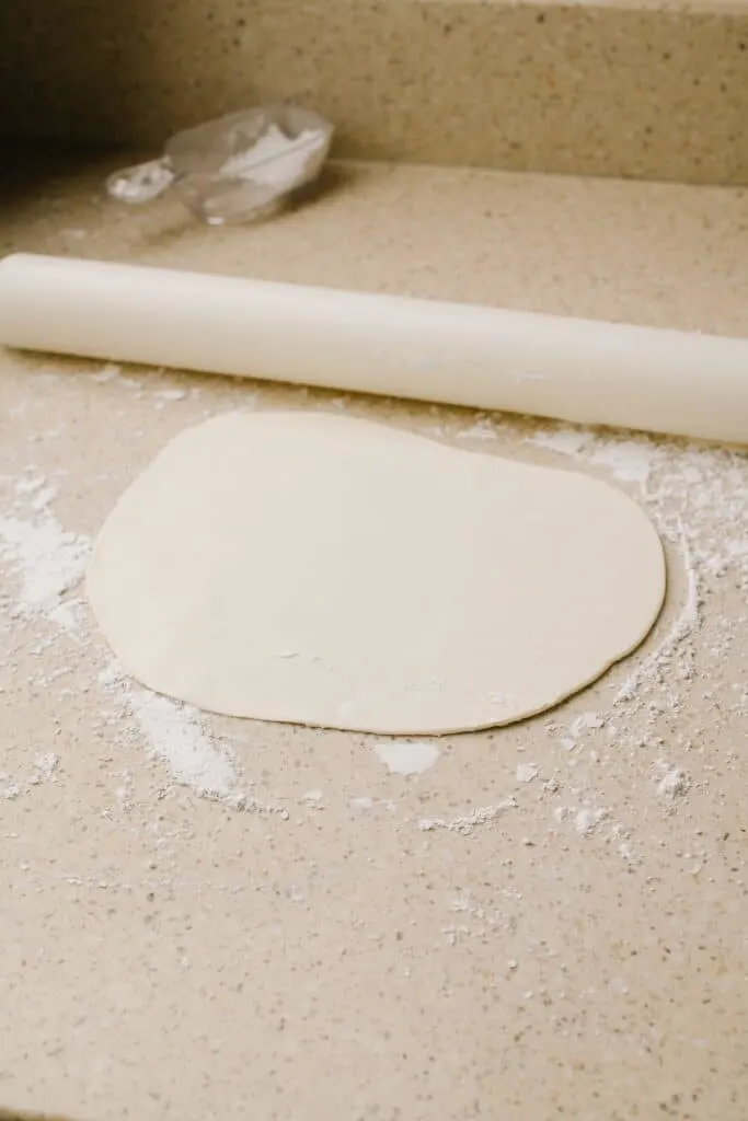 Sugar cookie dough, rolled out on a flour-coated surface, ready to be cut into shapes.