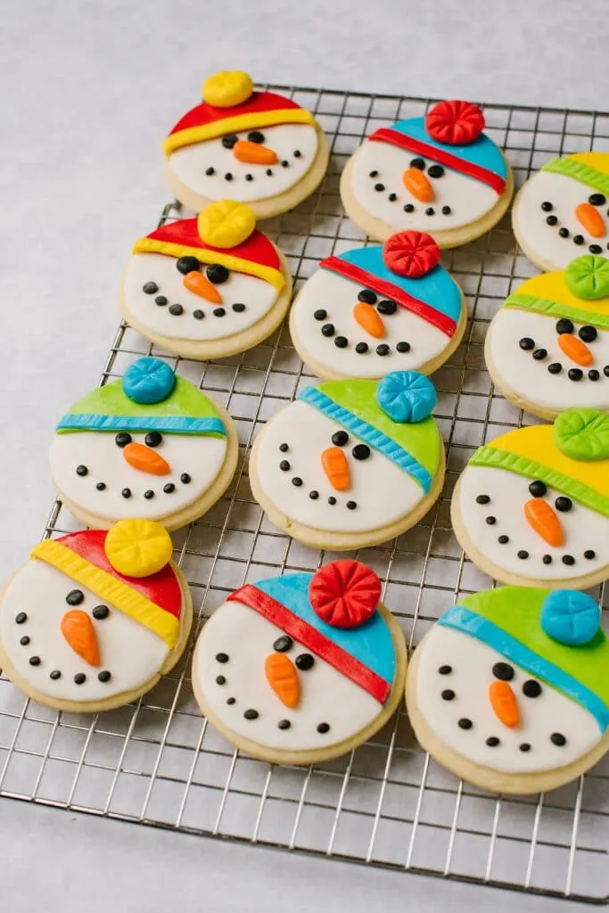 12 sugar cookies, decorated as snowmen, on a cooling rack.